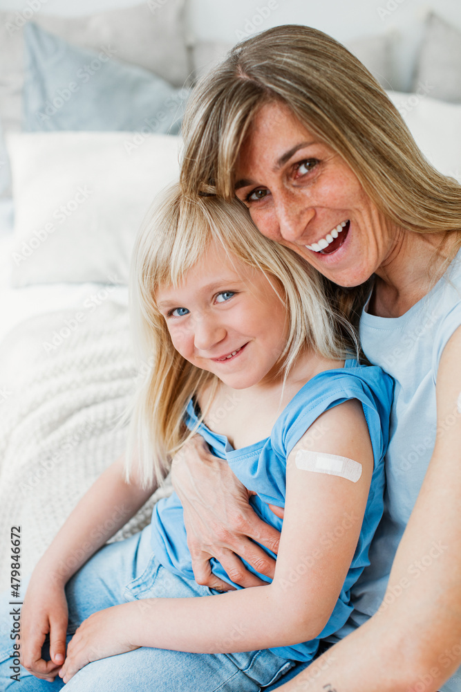 Mother and daughter laugh into the camera with fresh vaccination and plaster. Mother and daughter laugh into the camera with fresh vaccination and plaster.