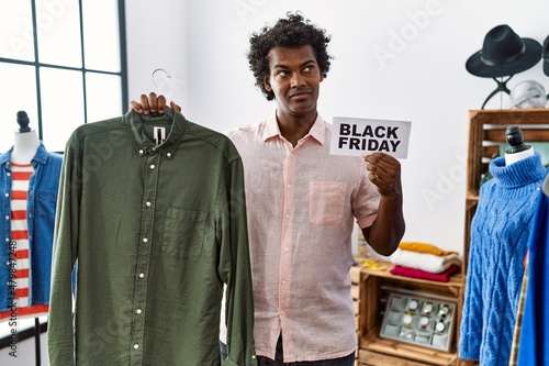 African man with curly hair holding black friday banner at retail shop smiling looking to the side and staring away thinking.