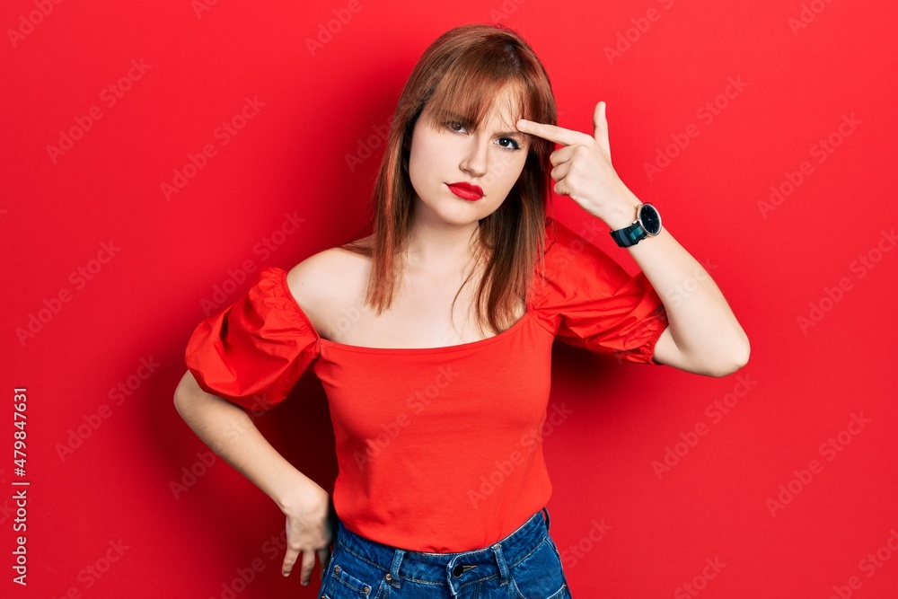 Redhead young woman wearing casual red t shirt pointing unhappy to pimple on forehead, ugly infection of blackhead. acne and skin problem Redhead young woman wearing casual red t shirt pointing unhappy to pimple on forehead, ugly infection of blackhead. acne and skin problem
