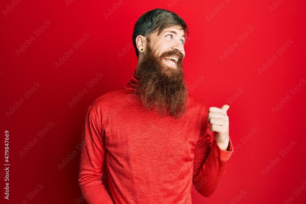 Redhead man with long beard wearing casual clothes pointing thumb up to the side smiling happy with open mouth Redhead man with long beard wearing casual clothes pointing thumb up to the side smiling happy with open mouth