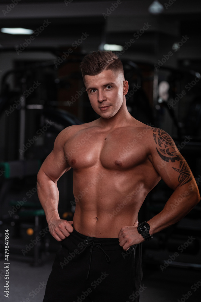 handsome sexy man with a hairstyle and a sporty naked body does training in the gym. Strong healthy guy looks at the camera