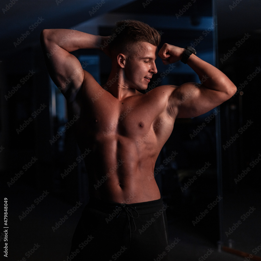 Handsome young sports man with a sexy naked torso and muscles in the gym on a dark background Handsome young sports man with a sexy naked torso and muscles in the gym on a dark background