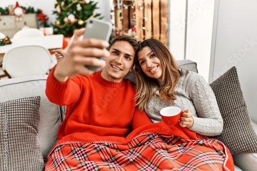 Young couple using smartphone and drinking coffee. Sitting on the sofa at home.