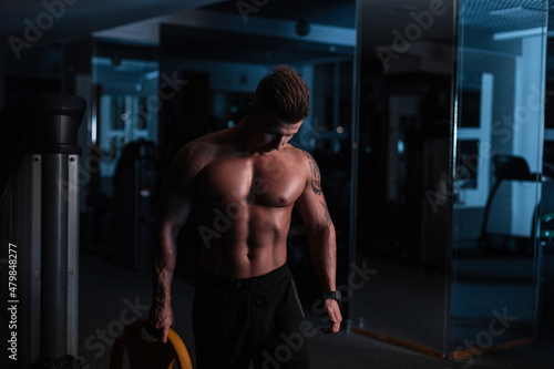 Sport. Young athletic man doing workout in the dark. Muscular and strong guy exercising.