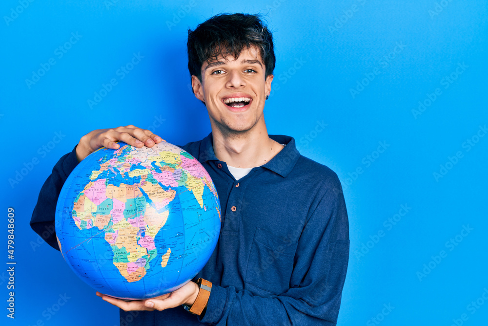 Handsome hipster young man holding world ball smiling with a happy and cool smile on face. showing teeth. Handsome hipster young man holding world ball smiling with a happy and cool smile on face. showing teeth.