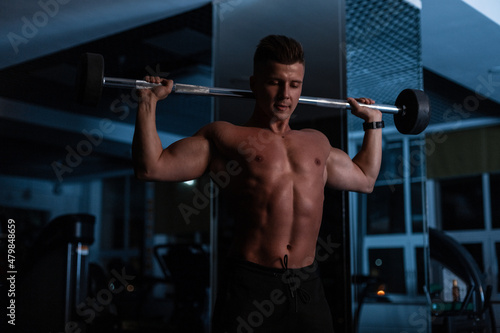 Bodybuilder man athlete with muscular body doing exercise in the hall on a dark blue background