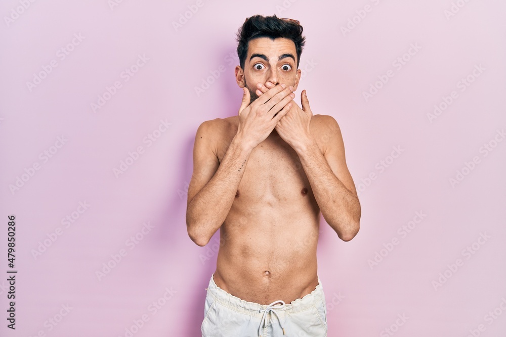 Fototapeta premium Young hispanic man wearing swimwear shirtless shocked covering mouth with hands for mistake. secret concept.