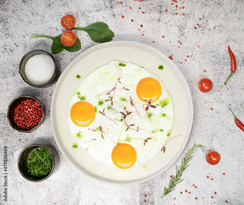 Breakfast. fried eggs from three eggs are sprinkled with grass on a light plate. next to seasonings and spices. High quality photo Breakfast. fried eggs from three eggs are sprinkled with grass on a light plate. next to seasonings and spices. High quality photo