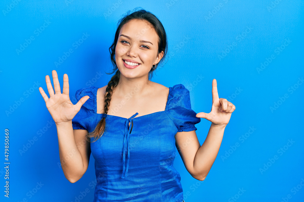 Fototapeta premium Young hispanic girl wearing casual clothes showing and pointing up with fingers number seven while smiling confident and happy.