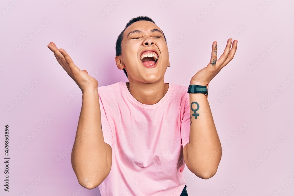 Beautiful hispanic woman with short hair wearing casual pink t shirt celebrating mad and crazy for success with arms raised and closed eyes screaming excited. winner concept Beautiful hispanic woman with short hair wearing casual pink t shirt celebrating mad and crazy for success with arms raised and closed eyes screaming excited. winner concept