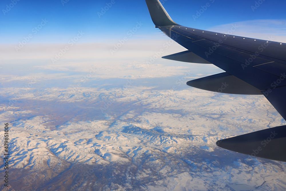 Obraz premium View to the wing of airplane in the sky and snowy mountains. Travel and transportation concept
