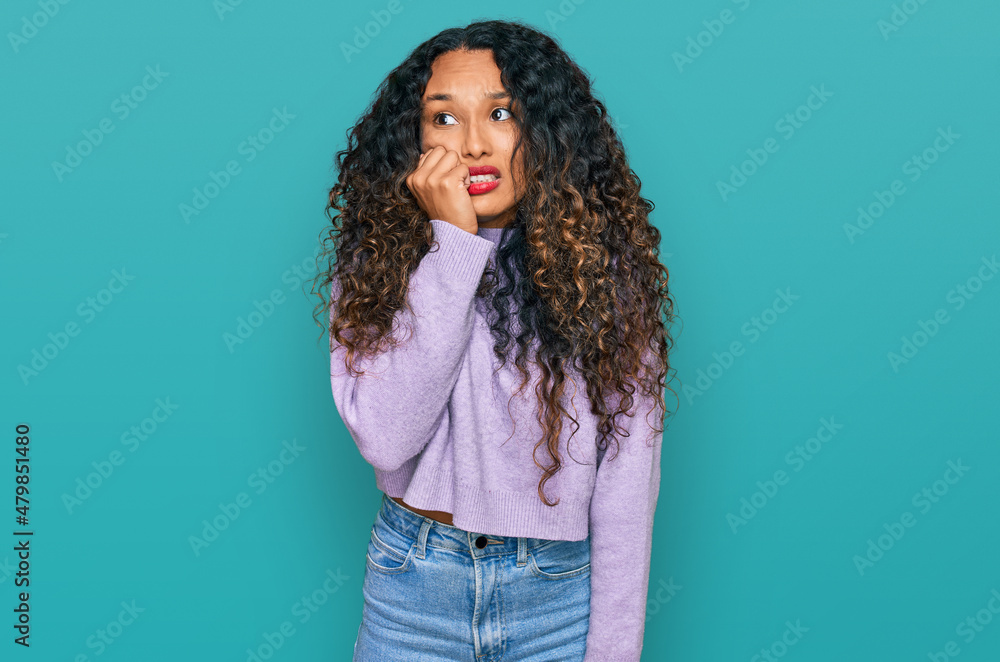 Young hispanic woman with curly hair wearing casual winter sweater looking stressed and nervous with hands on mouth biting nails. anxiety problem. Young hispanic woman with curly hair wearing casual winter sweater looking stressed and nervous with hands on mouth biting nails. anxiety problem.