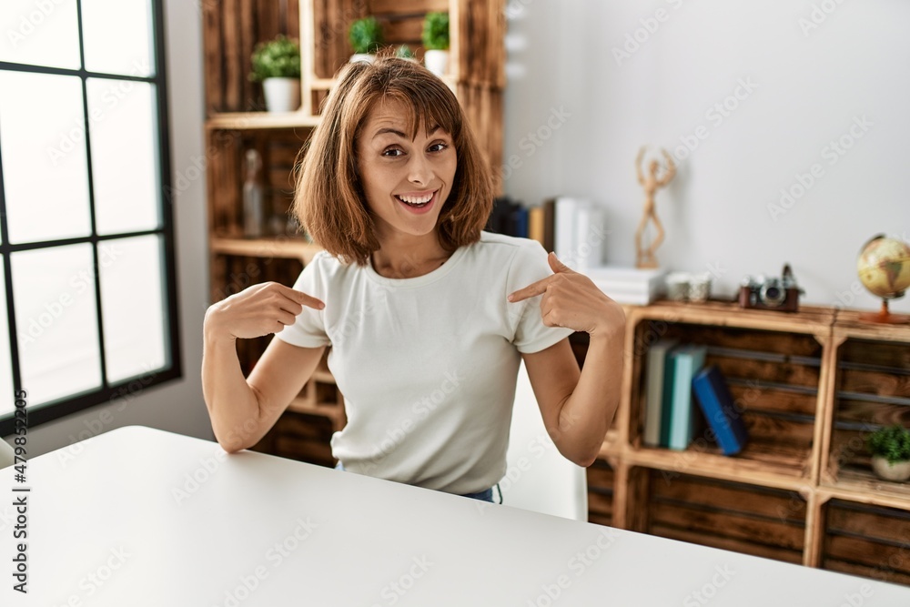 Young caucasian girl wearing casual clothes sitting on the table at home looking confident with smile on face, pointing oneself with fingers proud and happy. Young caucasian girl wearing casual clothes sitting on the table at home looking confident with smile on face, pointing oneself with fingers proud and happy.