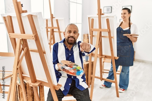Senior artist man at art studio pointing to you and the camera with fingers, smiling positive and cheerful