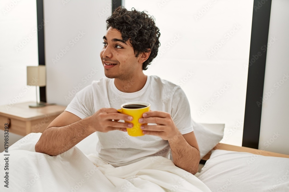 Young hispanic man drinking coffee sitting on the bed at bedroom. Young hispanic man drinking coffee sitting on the bed at bedroom.