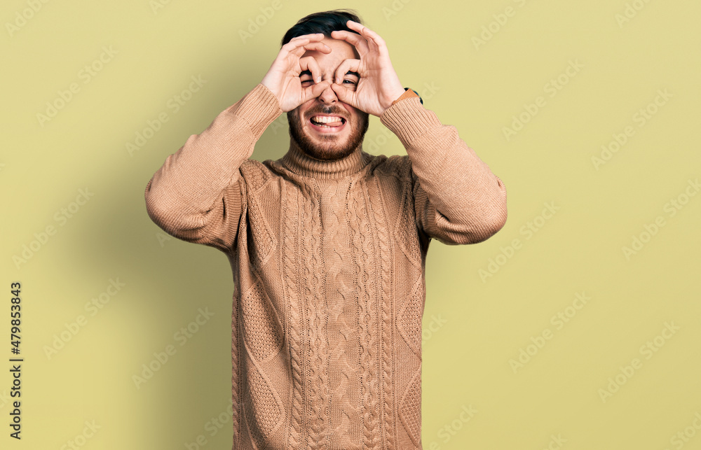 Young hispanic man wearing casual clothes doing ok gesture like binoculars sticking tongue out, eyes looking through fingers. crazy expression. Young hispanic man wearing casual clothes doing ok gesture like binoculars sticking tongue out, eyes looking through fingers. crazy expression.