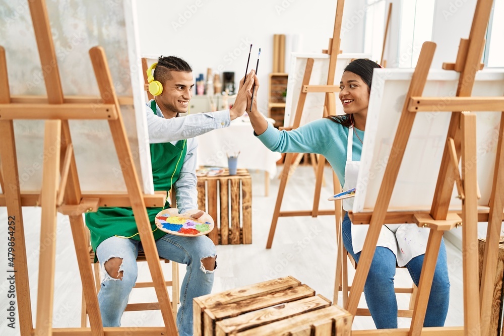 Young latin painter couple high five painting and using headphones at art studio Young latin painter couple high five painting and using headphones at art studio