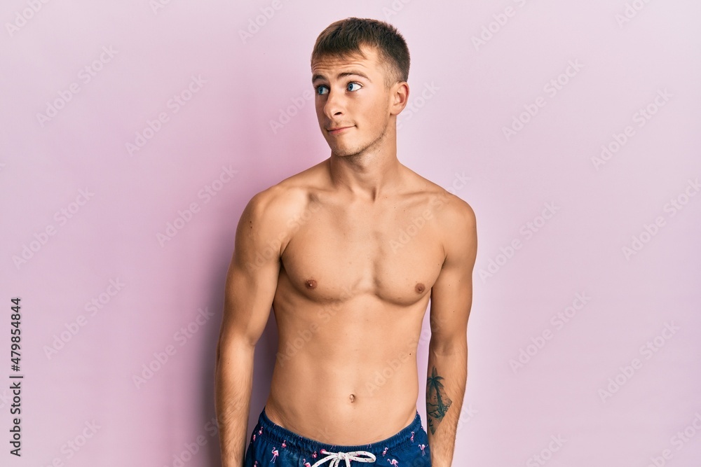 Young caucasian man wearing swimwear smiling looking to the side and staring away thinking.