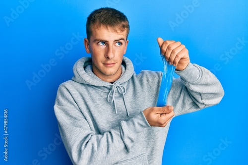 Young caucasian man holding slime smiling looking to the side and staring away thinking.