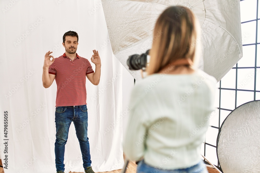 Fototapeta premium Woman photographer talking pictures of man posing as model at photography studio relax and smiling with eyes closed doing meditation gesture with fingers. yoga concept.
