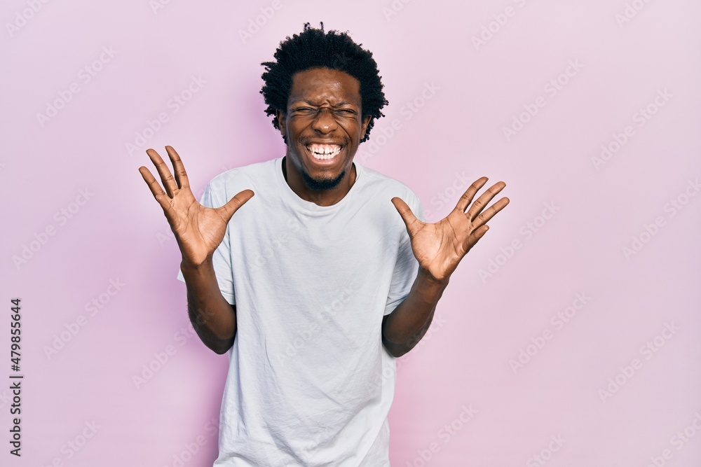 Young african american man wearing casual white t shirt celebrating mad and crazy for success with arms raised and closed eyes screaming excited. winner concept Young african american man wearing casual white t shirt celebrating mad and crazy for success with arms raised and closed eyes screaming excited. winner concept