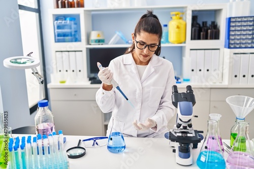 Young hispanic woman wearing scientist uniform using pipette working at laboratory