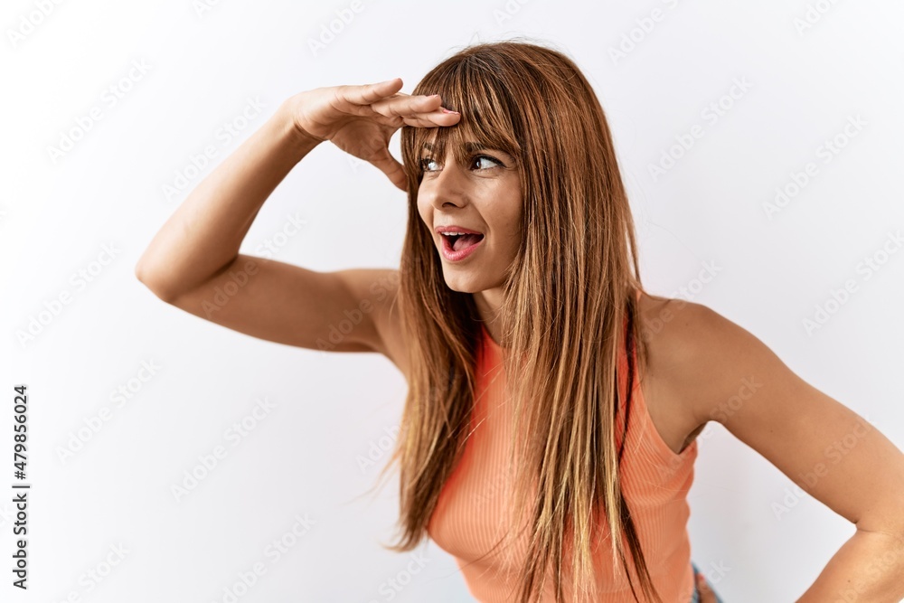 Fototapeta premium Hispanic woman with bang hairstyle standing over isolated background very happy and smiling looking far away with hand over head. searching concept.
