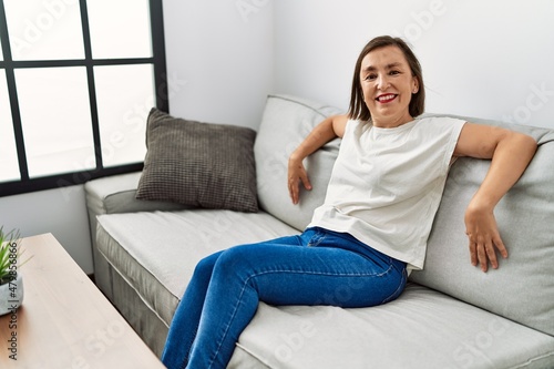 Middle age hispanic woman smiling sitting on the sofa at home
