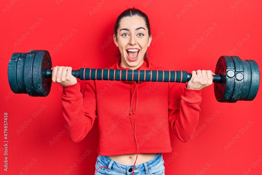 Obraz premium Beautiful woman with blue eyes wearing sportswear using dumbbells celebrating crazy and amazed for success with open eyes screaming excited.