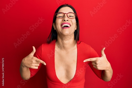 Young latin woman wearing casual clothes and glasses looking confident with smile on face, pointing oneself with fingers proud and happy.