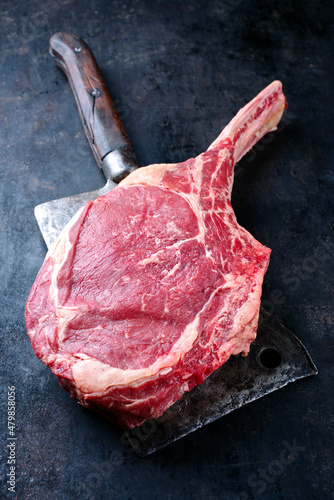 Raw dry aged chianina tomahawk steak as close-up on a cleaver on black rustic background with copy space photo