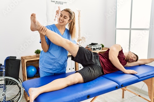 Young hispanic physioterapist woman make legs rehab treatment to man at the clinic. photo