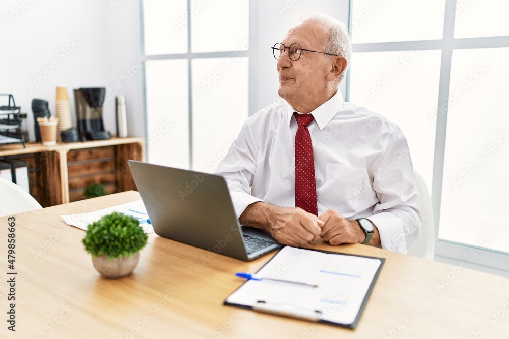 Senior man working at the office using computer laptop smiling looking to the side and staring away thinking. Senior man working at the office using computer laptop smiling looking to the side and staring away thinking.