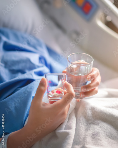 Asian woman patient with medical drip or IV drip holding water with medicine in hospital ward, Selective focus, Healthcare concept.
