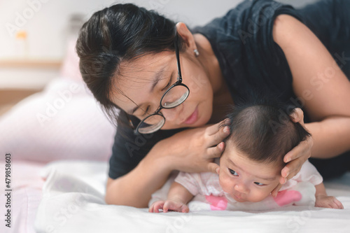 фотографія Little two month asian baby lying on stomach and try raised her neck, Asian mother come to help her daughter,  Family concept