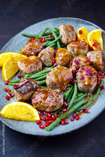 Modern style jusy seared pork pigllet tenderloin fillet meat medallions with orange relish sauce, pomegranate and green baby beans vegetable served as close-up on a Nordic design plate photo