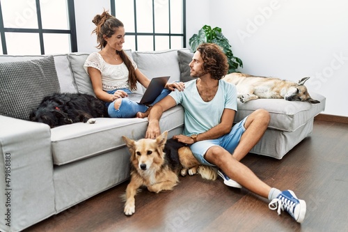 Young hispanic couple with dogs relaxing at home looking to side, relax profile pose with natural face and confident smile.