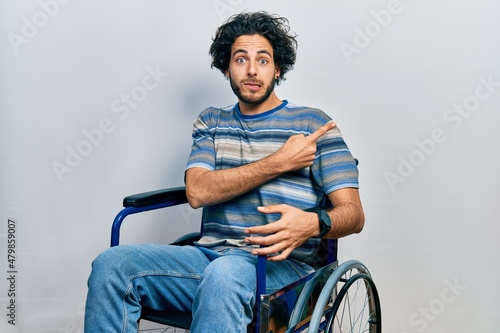 Handsome hispanic man sitting on wheelchair pointing aside worried and nervous with forefinger, concerned and surprised expression