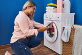 Young hispanic woman using smartphone waiting for washing machine at laundry room