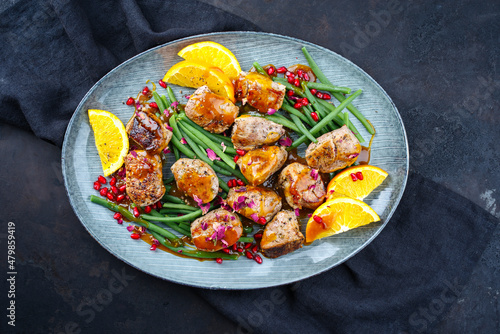 Modern style jusy seared pork pigllet tenderloin fillet meat medallions with orange relish sauce, pomegranate and green baby beans vegetable served as close-up on a Nordic design plate