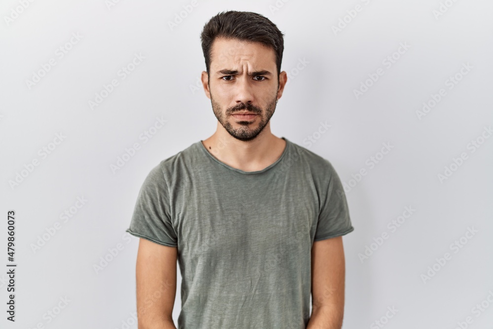 Young hispanic man with beard wearing casual t shirt over white background skeptic and nervous, frowning upset because of problem. negative person. Young hispanic man with beard wearing casual t shirt over white background skeptic and nervous, frowning upset because of problem. negative person.