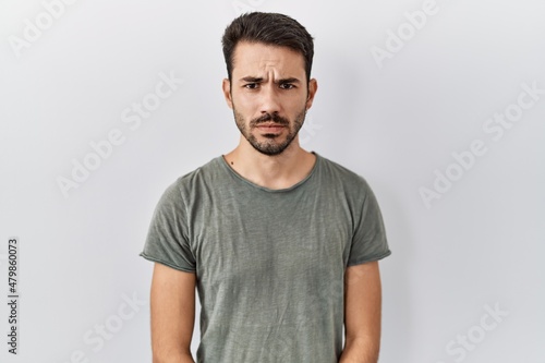 Young hispanic man with beard wearing casual t shirt over white background skeptic and nervous, frowning upset because of problem. negative person.