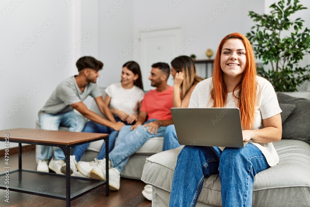 Group of young friends speaking sitting on the sofa. Woman smilimg happy and using laptop at home. Group of young friends speaking sitting on the sofa. Woman smilimg happy and using laptop at home.