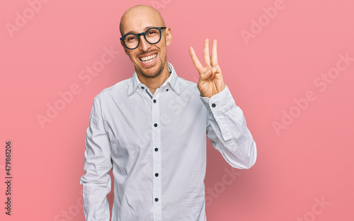 Bald man with beard wearing business shirt and glasses showing and pointing up with fingers number three while smiling confident and happy.