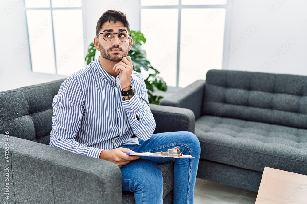 Young psychologist man at consultation office with hand on chin thinking about question, pensive expression. smiling with thoughtful face. doubt concept. Young psychologist man at consultation office with hand on chin thinking about question, pensive expression. smiling with thoughtful face. doubt concept.