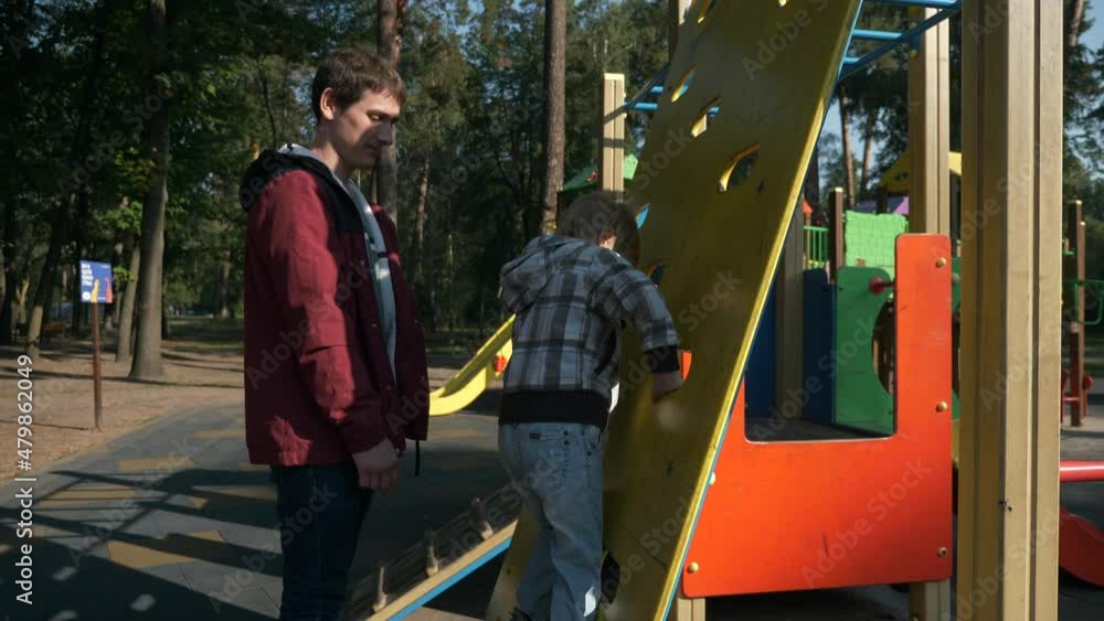 Man Watch Boy Climbing Ladder Wall Young Father with Child Kid Play on Playground. Bright Sunny Summer Day. Slow motion 4K Man Watch Boy Climbing Ladder Wall Young Father with Child Kid Play on Playground. Bright Sunny Summer Day. Slow motion 4K