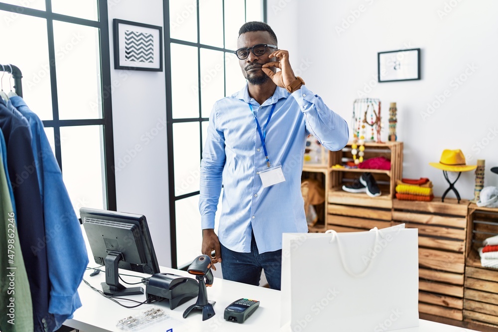 Young african man working as manager at retail boutique mouth and lips shut as zip with fingers. secret and silent, taboo talking Young african man working as manager at retail boutique mouth and lips shut as zip with fingers. secret and silent, taboo talking