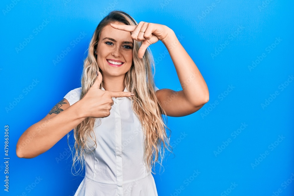 Beautiful young blonde woman wearing casual white shirt smiling making frame with hands and fingers with happy face. creativity and photography concept. Beautiful young blonde woman wearing casual white shirt smiling making frame with hands and fingers with happy face. creativity and photography concept.