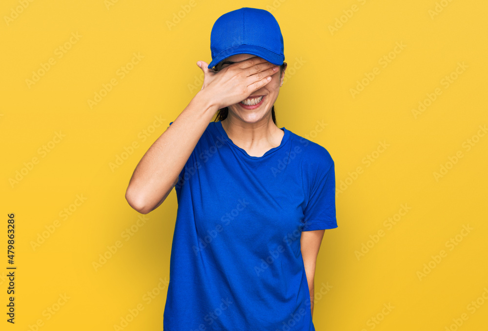 Young hispanic girl wearing delivery courier uniform smiling and laughing with hand on face covering eyes for surprise. blind concept.