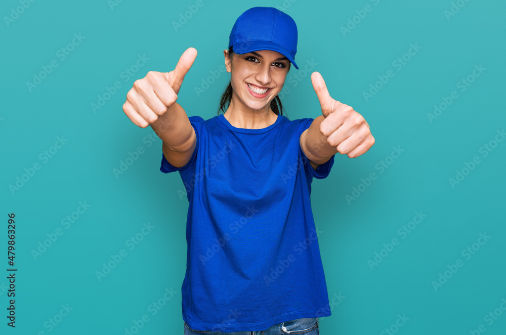 Young hispanic girl wearing delivery courier uniform approving doing positive gesture with hand, thumbs up smiling and happy for success. winner gesture.